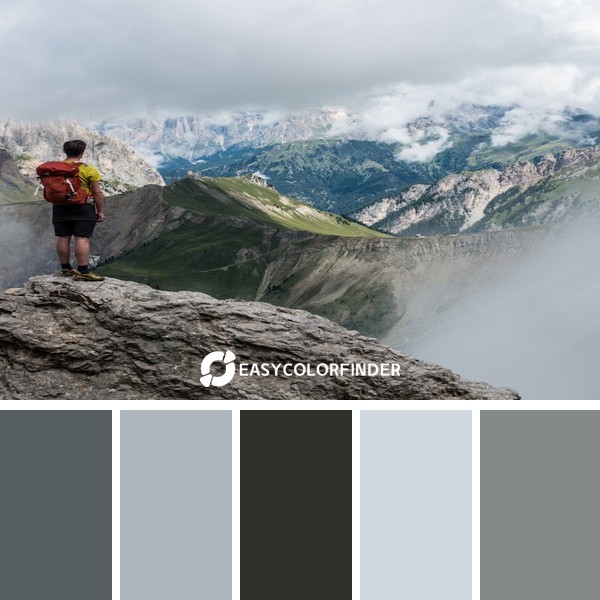 man with rbackpack standing on cliff facing mountains under white sky during daytime